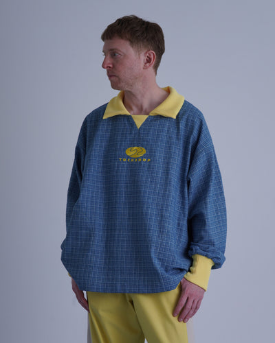 FOOTBALL POLO PULLOVERを着た男性の横向きの写真、青いチェック柄と黄色の襟が特徴