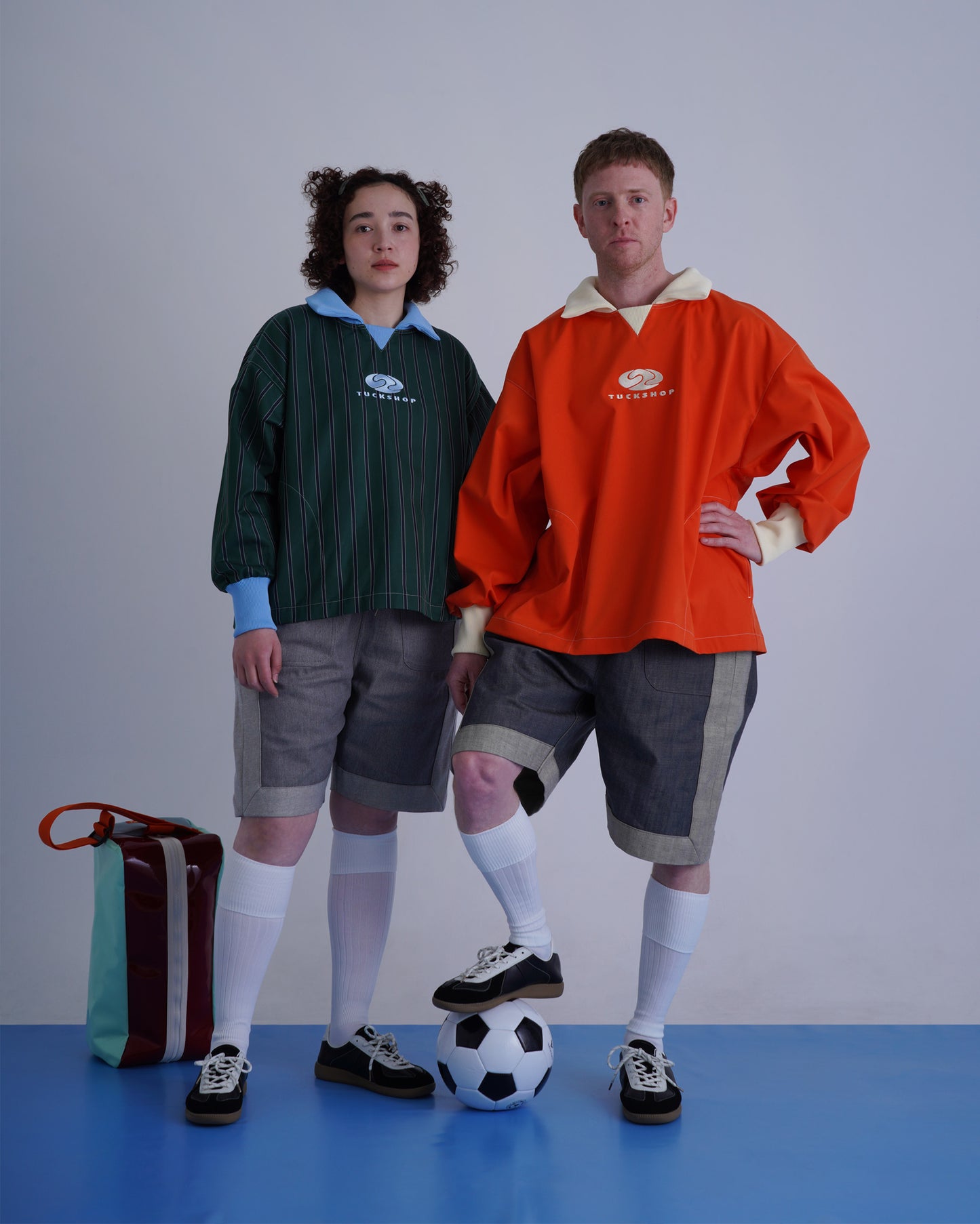 FOOTBALL POLO PULLOVERを着用した男女がサッカーボールを持ってポーズを取るシーンの画像