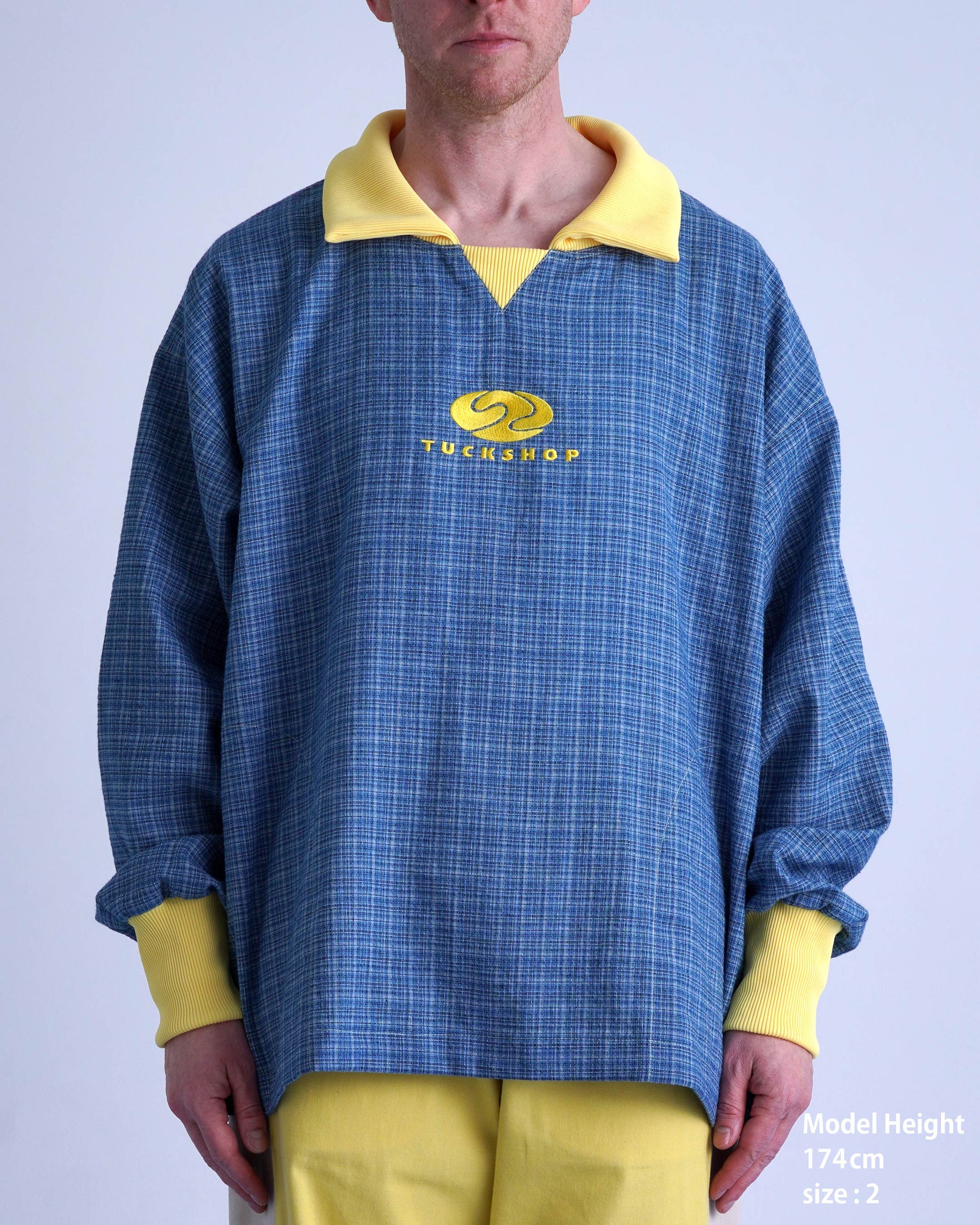FOOTBALL POLO PULLOVERを着用した男性モデル、青チェック柄で襟はイエロー、ロゴ刺繍入り