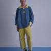 FOOTBALL POLO PULLOVERを着たモデルが立っている。青と黄色のコントラストが特徴。