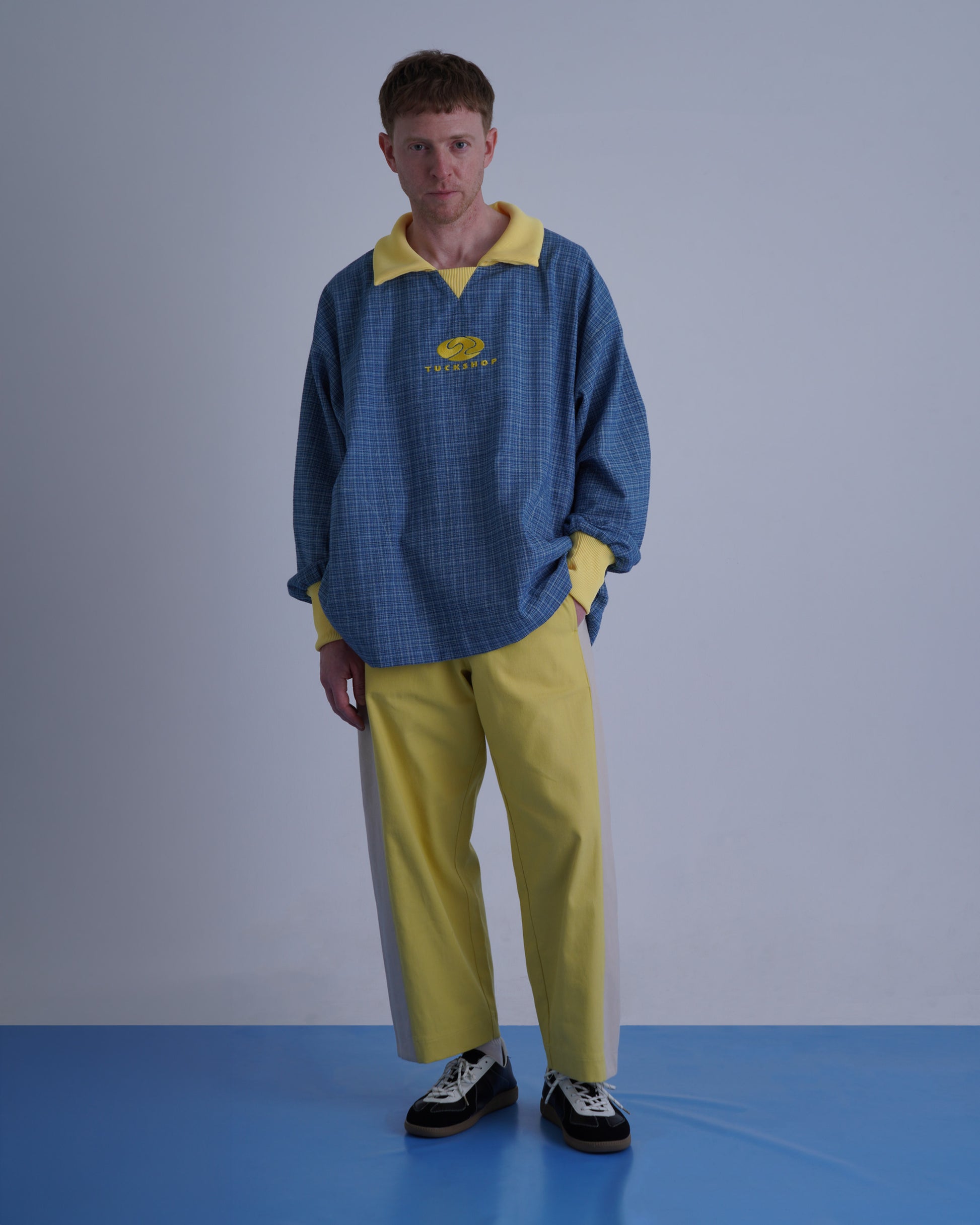 FOOTBALL POLO PULLOVERを着たモデルが立っている。青と黄色のコントラストが特徴。