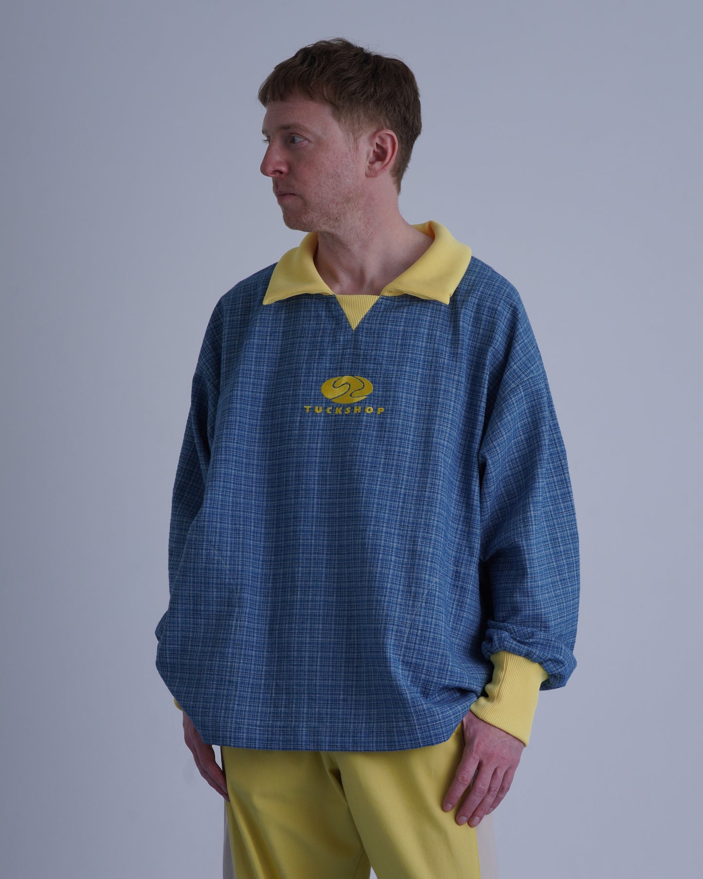 FOOTBALL POLO PULLOVERを着た男性の横向きの写真、青いチェック柄と黄色の襟が特徴