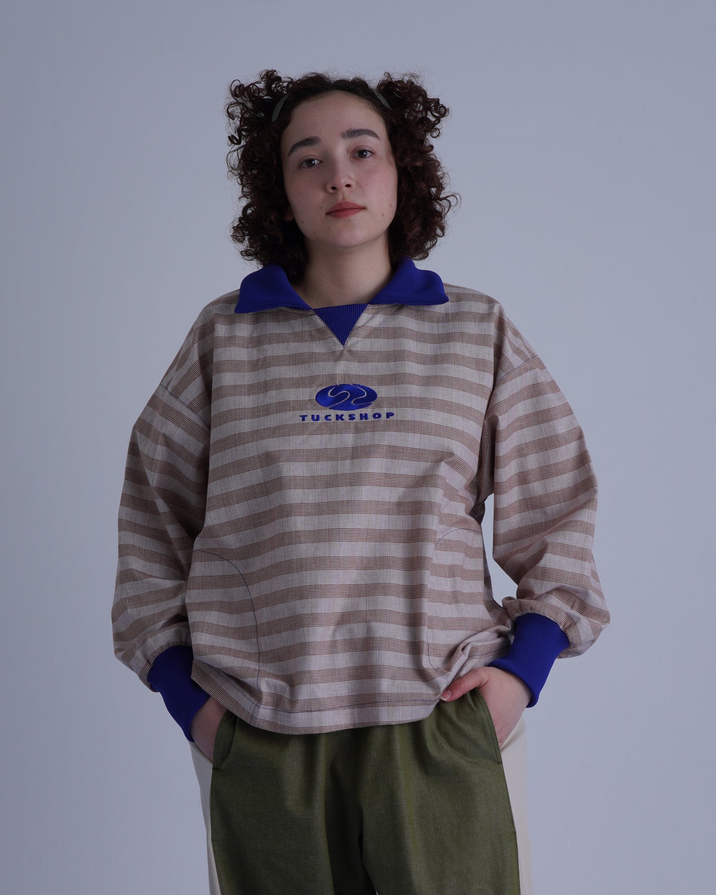 FOOTBALL POLO PULLOVERを着たモデルが、ストライプ柄のプルオーバーを着ています。青い襟とロゴ刺繍が特徴。