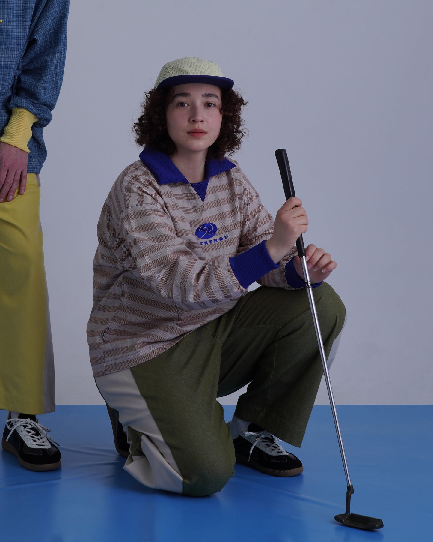 FOOTBALL POLO PULLOVERを着用した女性がゴルフクラブを持っている姿