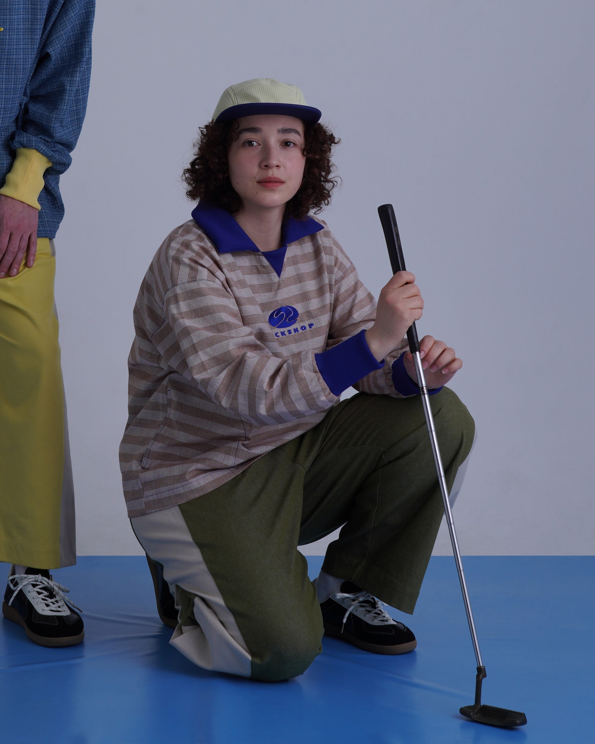 FOOTBALL POLO PULLOVERを着用した女性がゴルフクラブを持っている姿