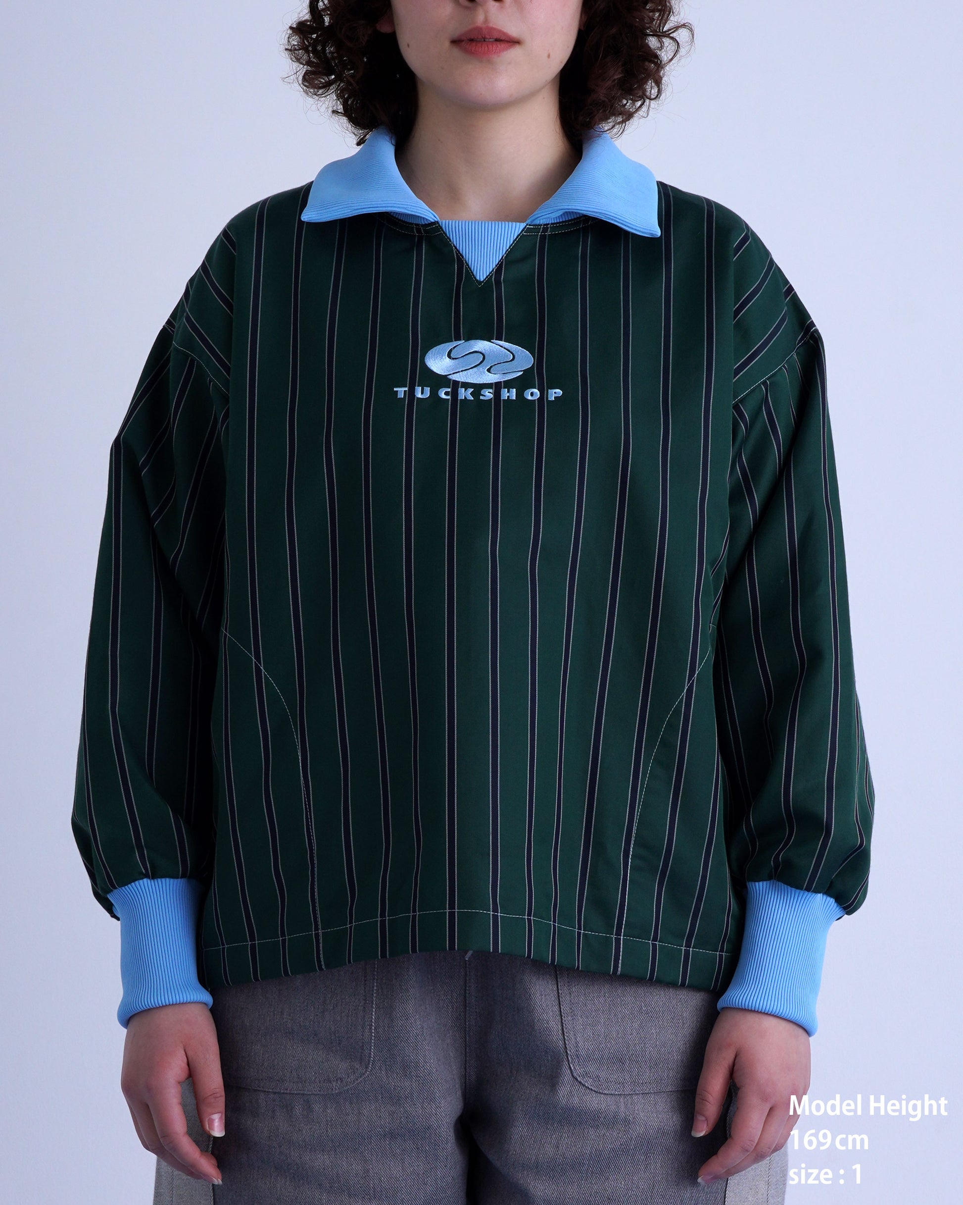 女性モデルが着用しているFOOTBALL POLO PULLOVER、ストライプデザイン、青い襟、ロゴ刺繍入り