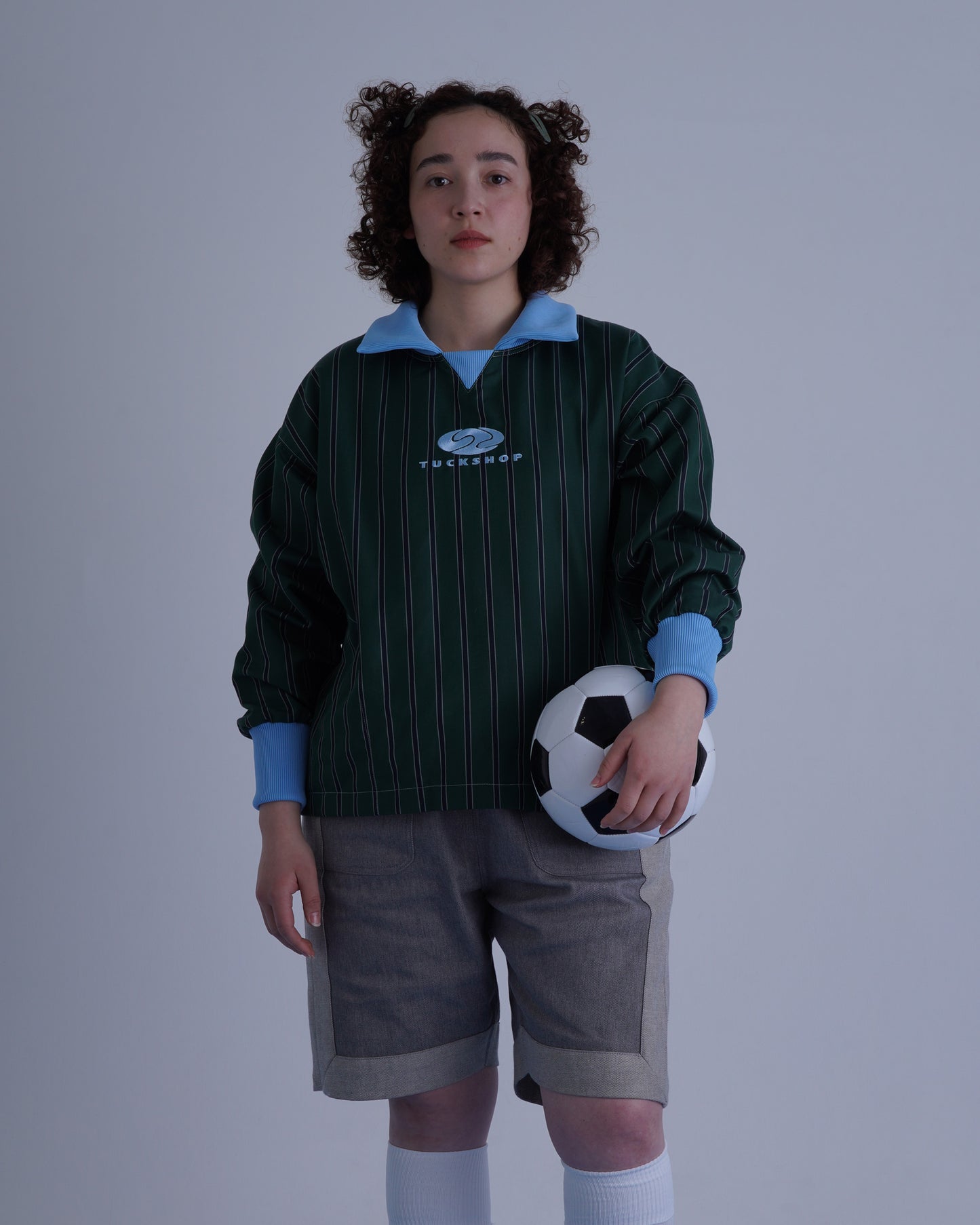 FOOTBALL POLO PULLOVERを着たモデルがサッカーボールを持っている写真。緑のストライプ柄のプルオーバー。