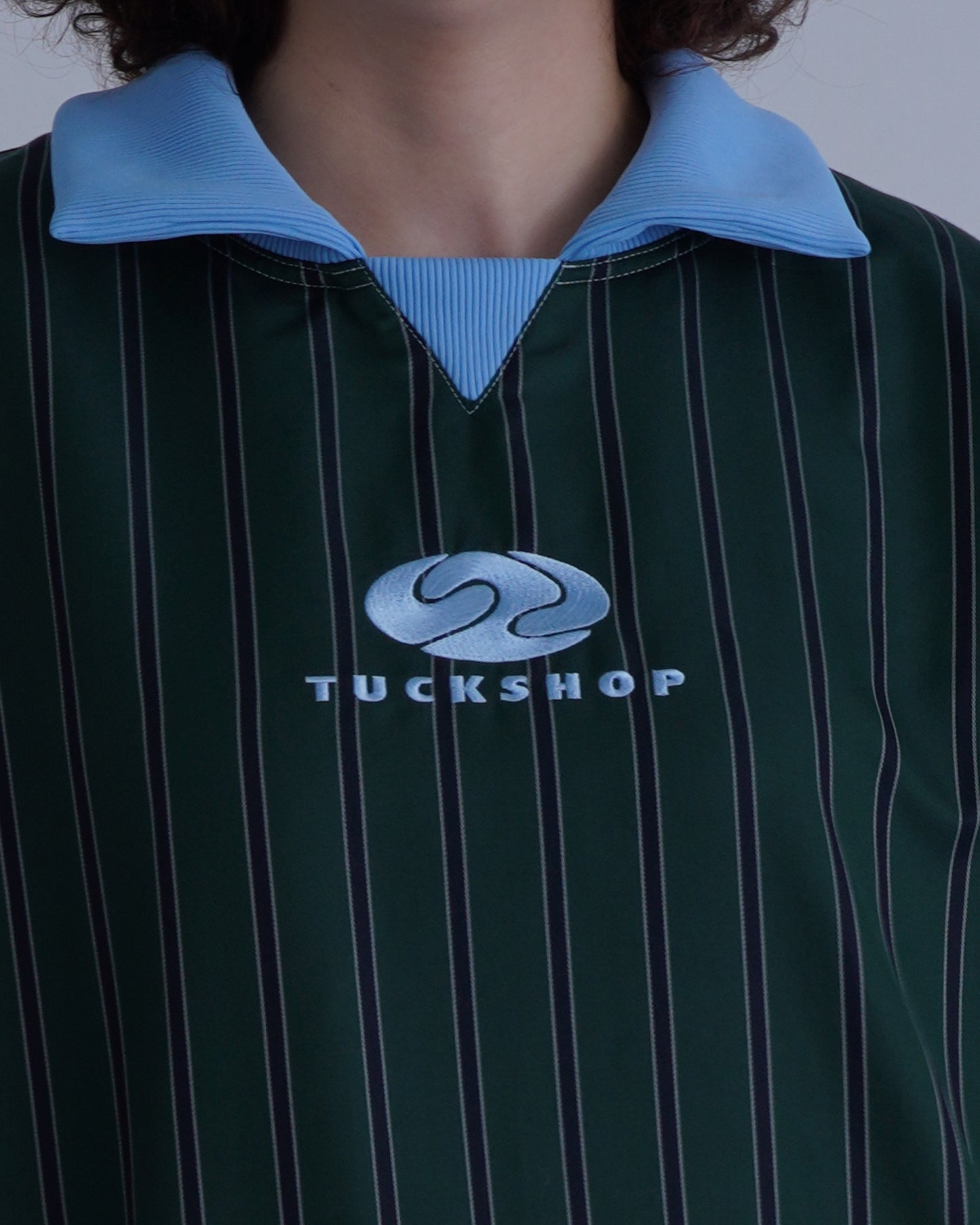 FOOTBALL POLO PULLOVERの緑色のストライプ柄で、青い襟とロゴ"TUCKSHOP"が特徴的。