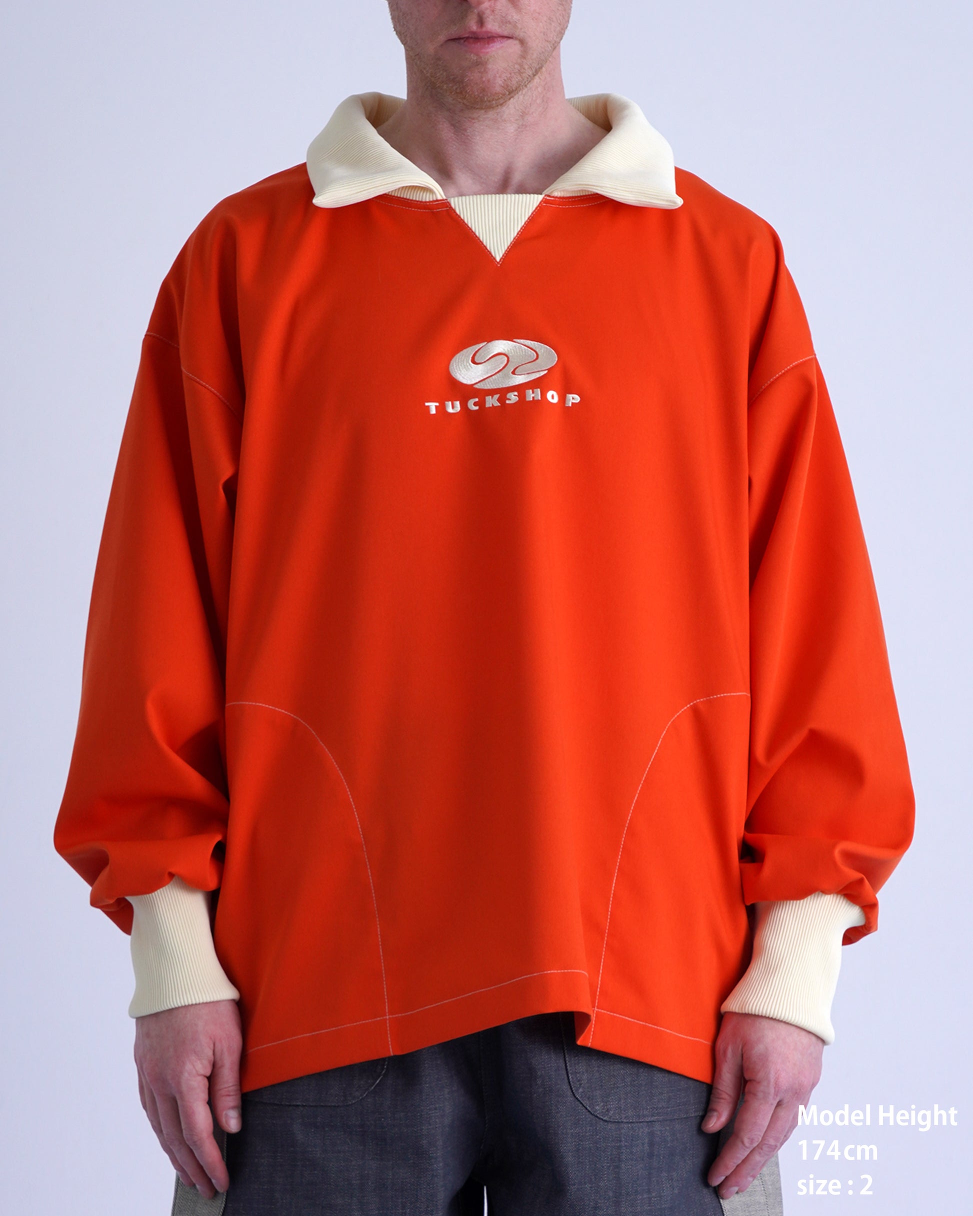 FOOTBALL POLO PULLOVERのオレンジ色プルオーバー、襟付きデザインとロゴ刺繍、モデル身長174cmでサイズ2。