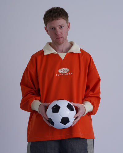 FOOTBALL POLO PULLOVERを着用し、サッカーボールを持つ男性の画像。オレンジ色のプルオーバー。