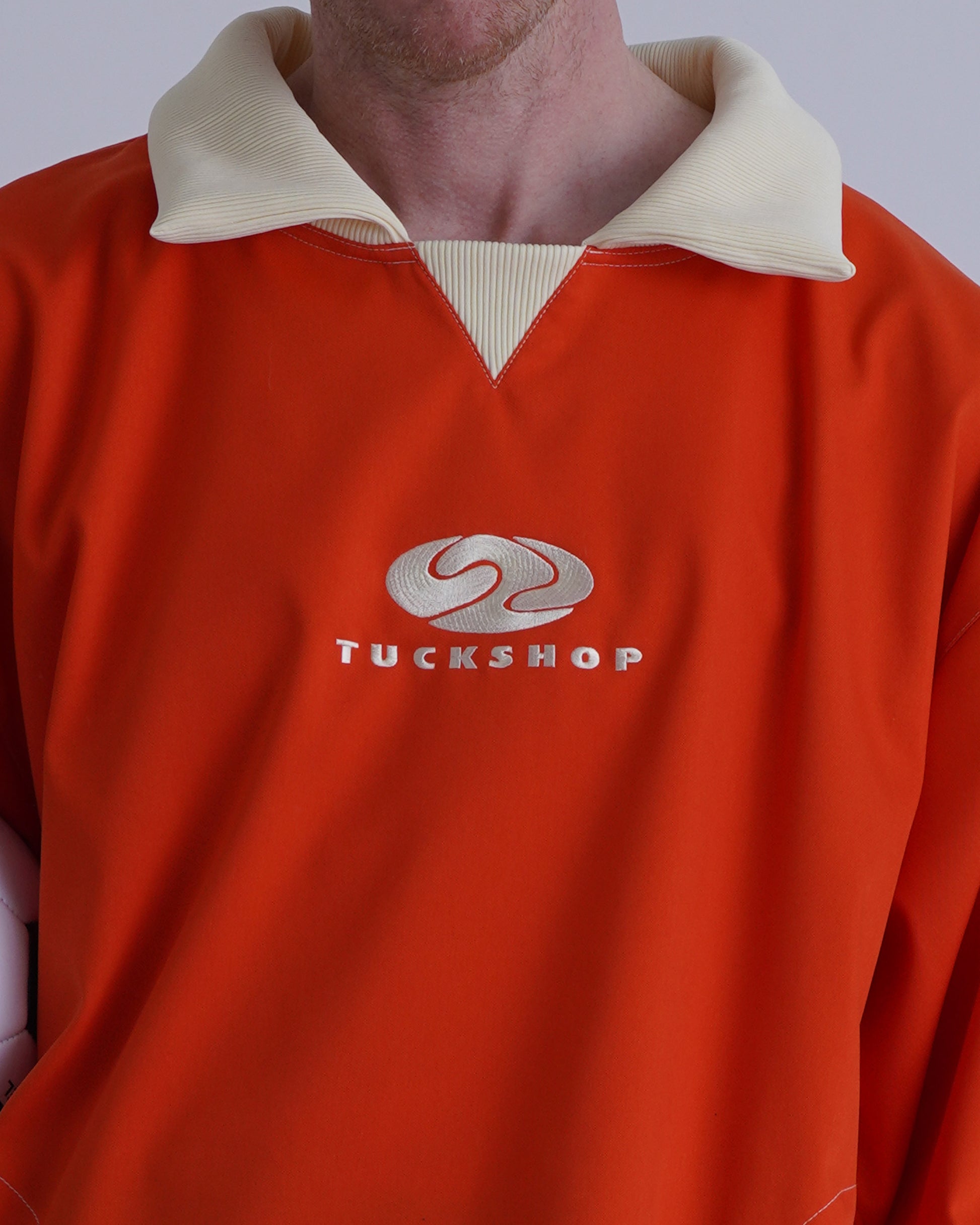 FOOTBALL POLO PULLOVER、オレンジ色の襟付きプルオーバーでTUCKSHOPロゴが胸に刺繍されている