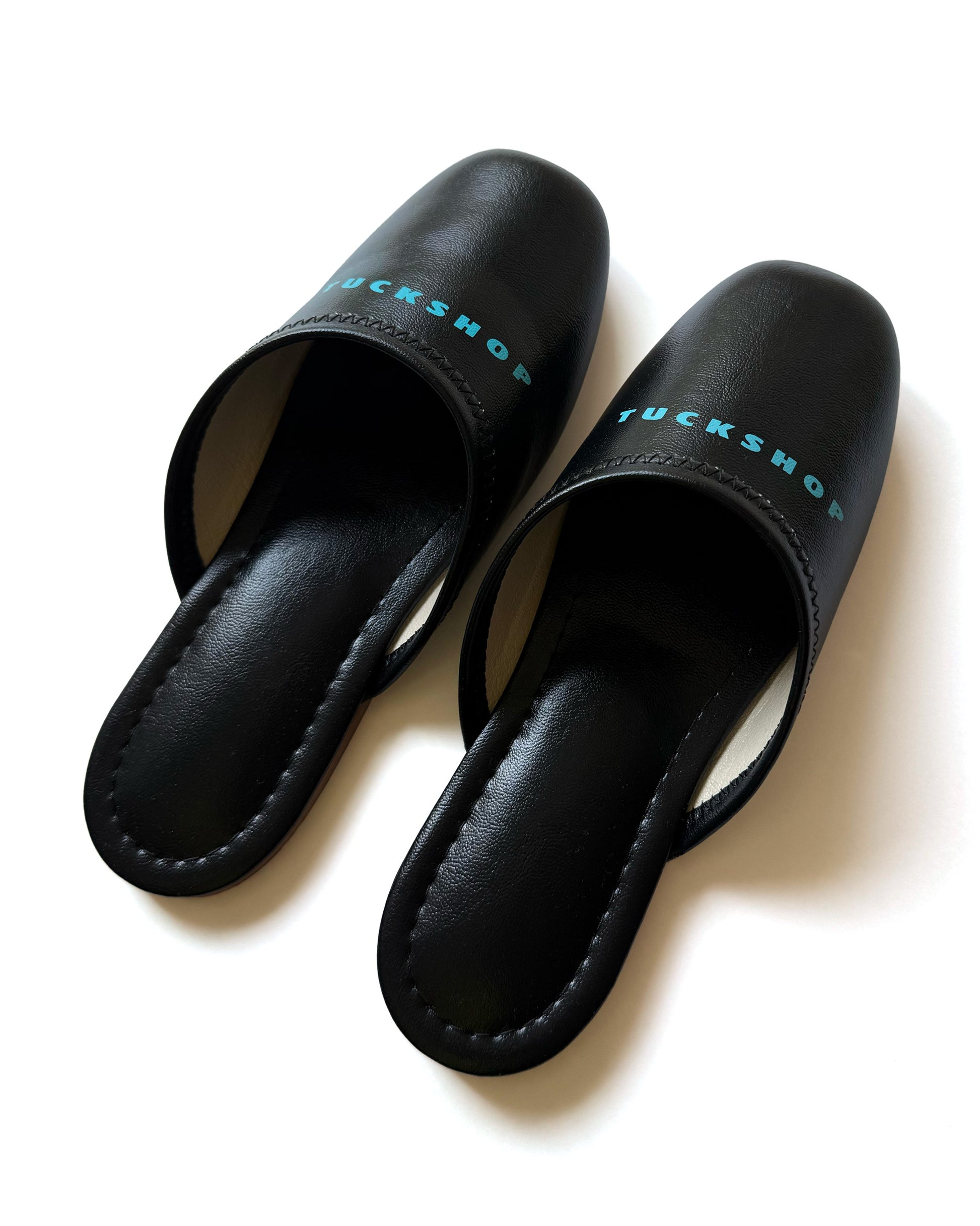 Black faux leather indoor slippers with logo print on instep, featuring a sleek design and comfortable fit.