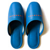 Blue faux leather indoor slippers with logo 'TUCKSHOP' printed on the instep.
