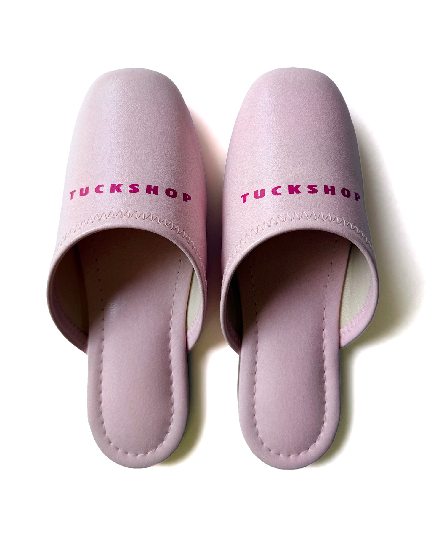 Pink faux leather slippers with TUCKSHOP logo on the instep, perfect for indoor use.