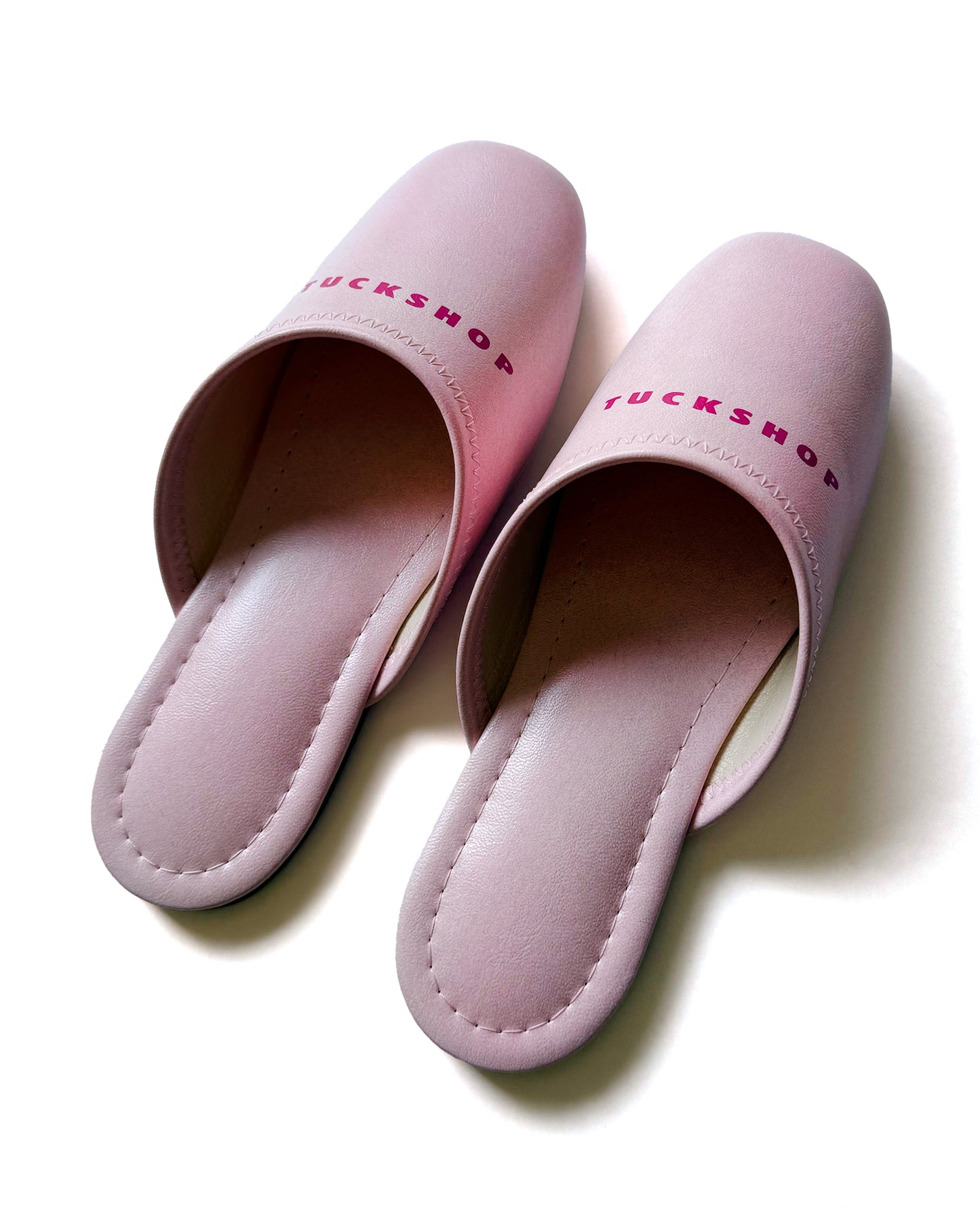 Pink faux leather slippers with 'TUCKSHOP' logo on instep, perfect for indoor use.